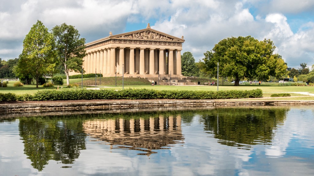 the parthenon on a sunny day, reflected in the rippling water beside it