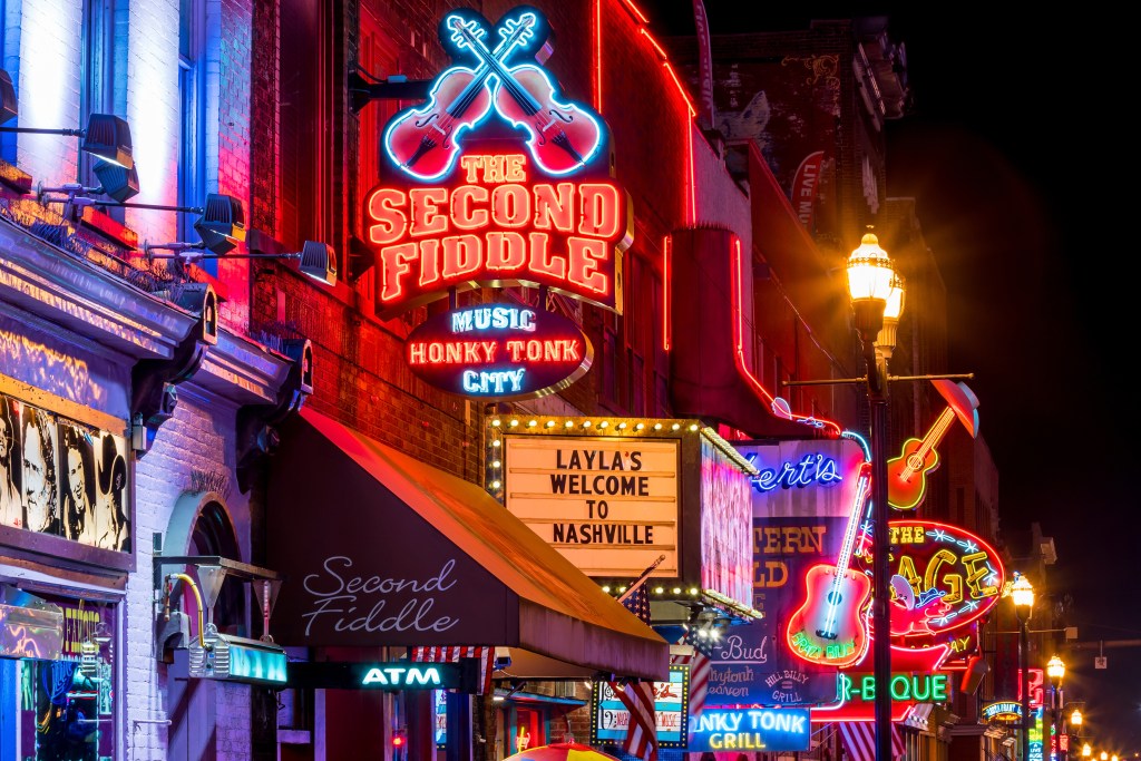 a section of lower Broadway street at night, with all of the bar neon signs running down the sides of the street