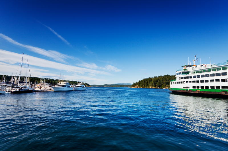 Image of bright blue sky and ocean with large ferry boat and smaller boats in a marina.
