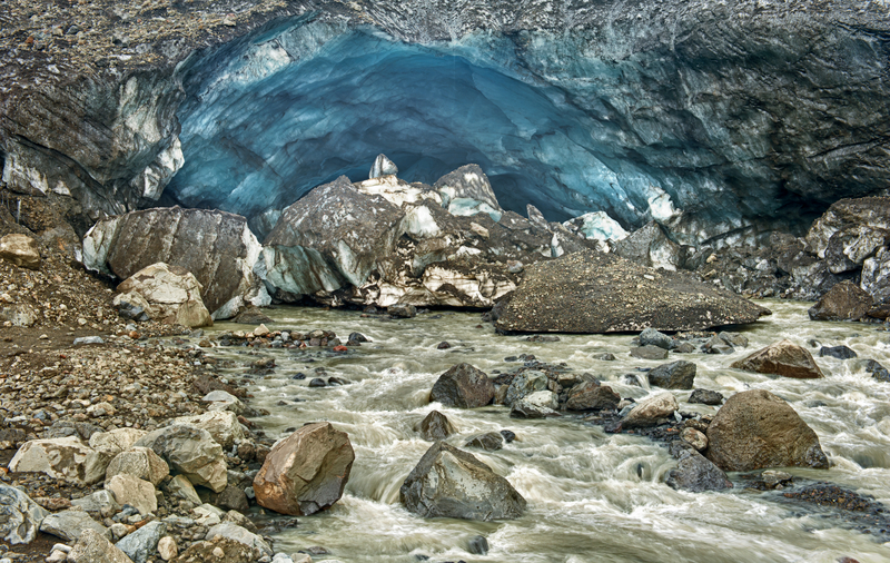 A rocky stream flowing from the entrance of a blue ice cave