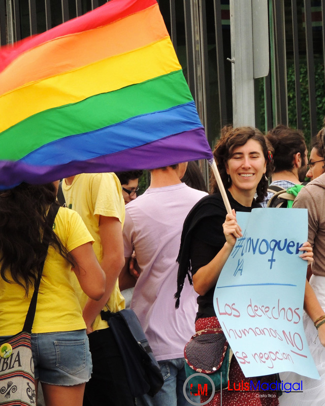 a demonstrator holding a pride flag and sign in spanish