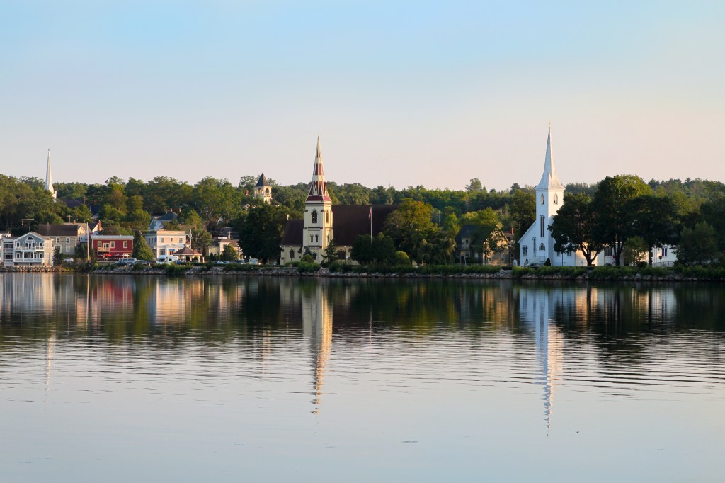 White steepled churches along the shore reflected in calm water.