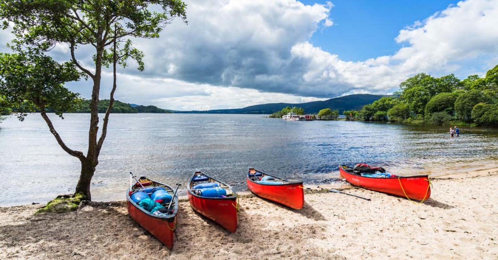 Four red kayaks resting on the sandy beach of Loch Lomond, Scotland.