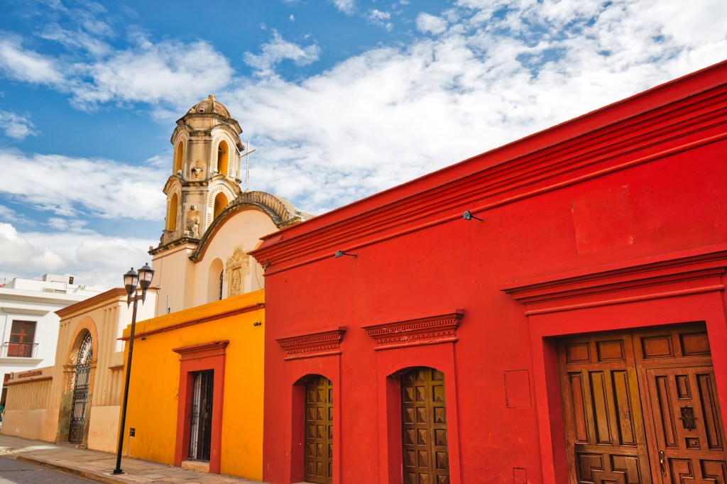 Image of street with colorful red and orange buildings and a tall stone church belltower.