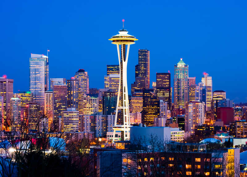 City skyline with tall buildings and Space Needle illuminated at night.