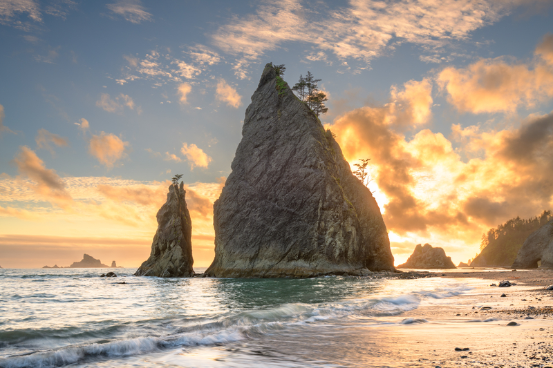 A beach with tall rock formations under sunset of golden clouds