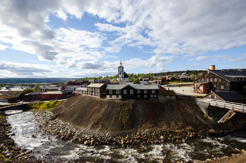 Image of wooden buildings perched on hill overlooking bend in river