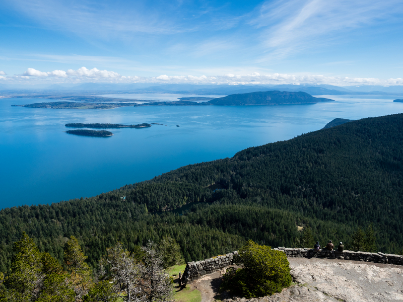 View from the top of a mountain looking out over forested slope and ocean stretching into the distance dotted with dark islands.